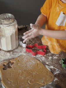  A young boy joyfully shapes gingerbread cookies on a kitchen counter, surrounded by flour and festive decorations.